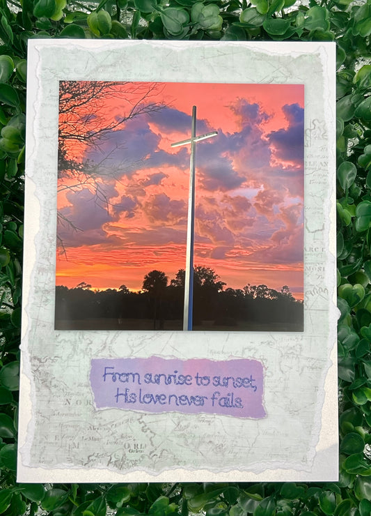 Card with a cross against a sunset sky and text 'From sunrise to sunset, His love never fails' on a textured white border.